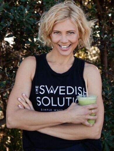 Kajsa Humphreys stands with crossed arms holding a green smoothie and wearing a Swedish Solution branded black singlet with white writing